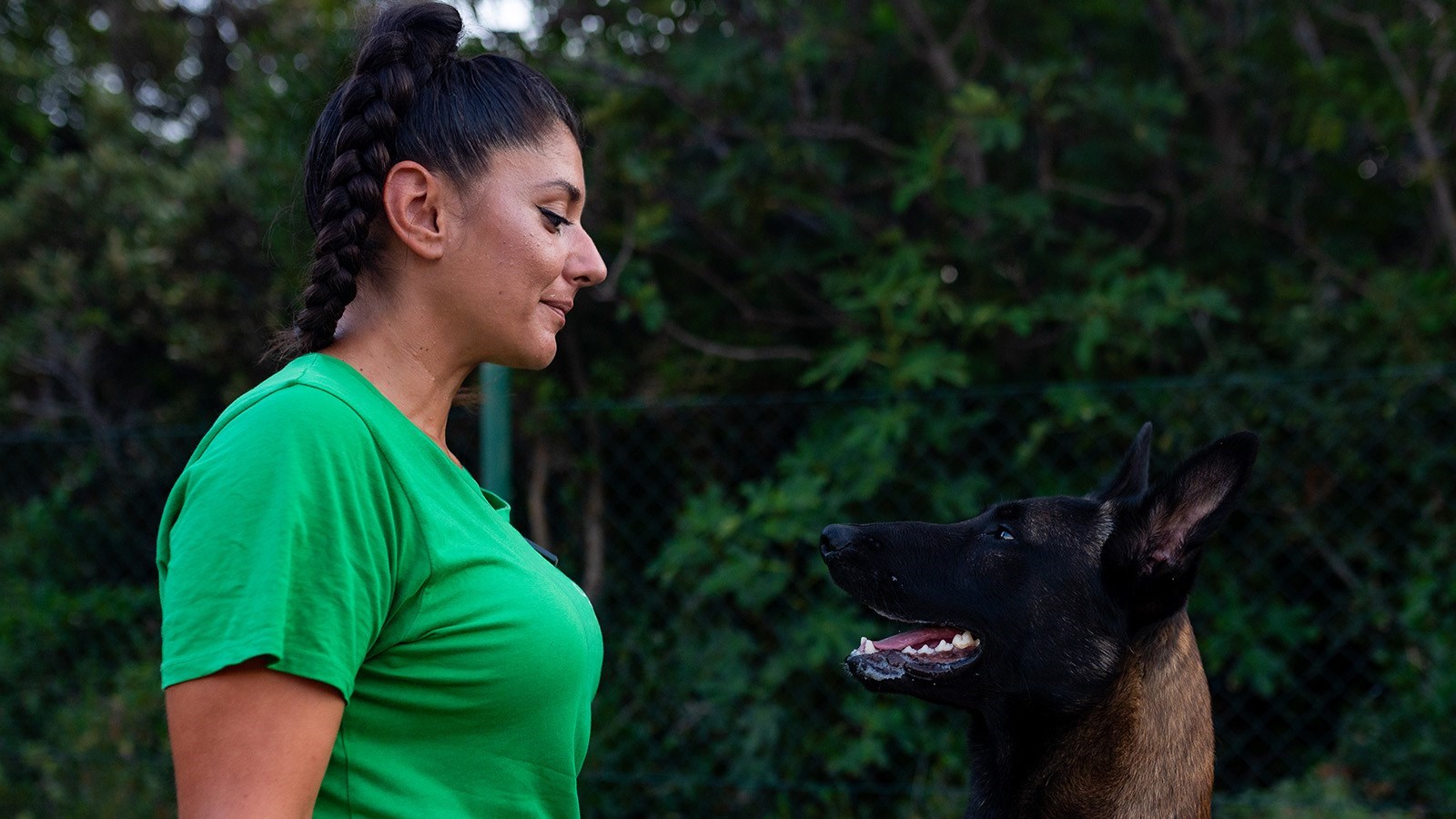 A woman in a green shirt looking at a dog outdoors